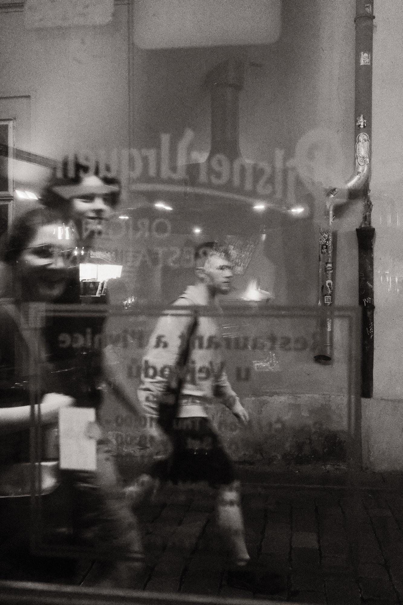 Čiernobiela fotografia mesta zachytáva ľudí kráčajúcich pre pražskou krčmou.