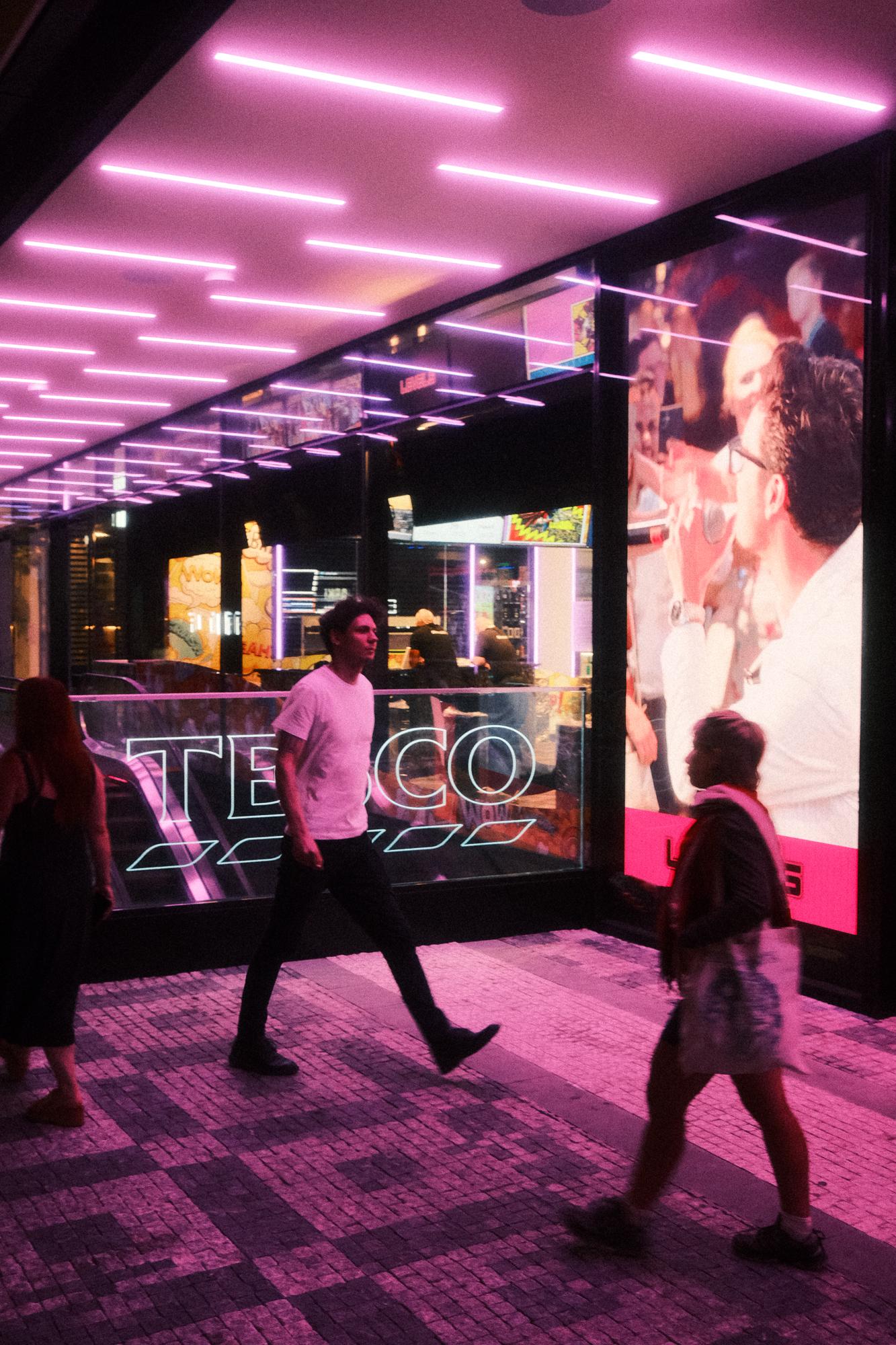 Nočná ulica nákupného centra s ružovým neónovým osvetlením.