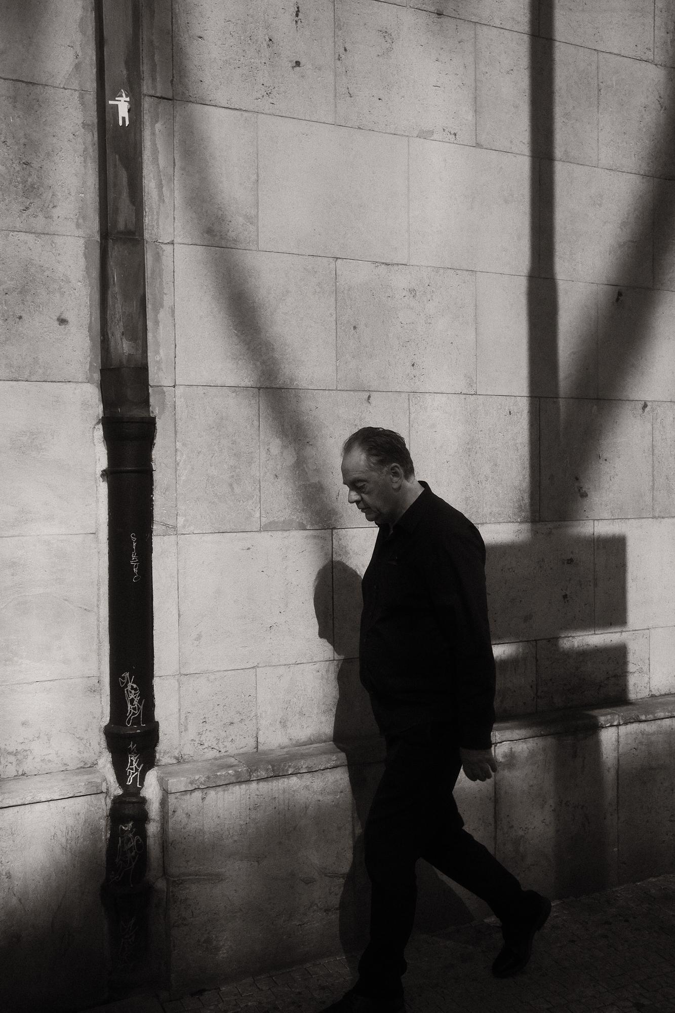 Muž kráča popri stene s tieňmi.