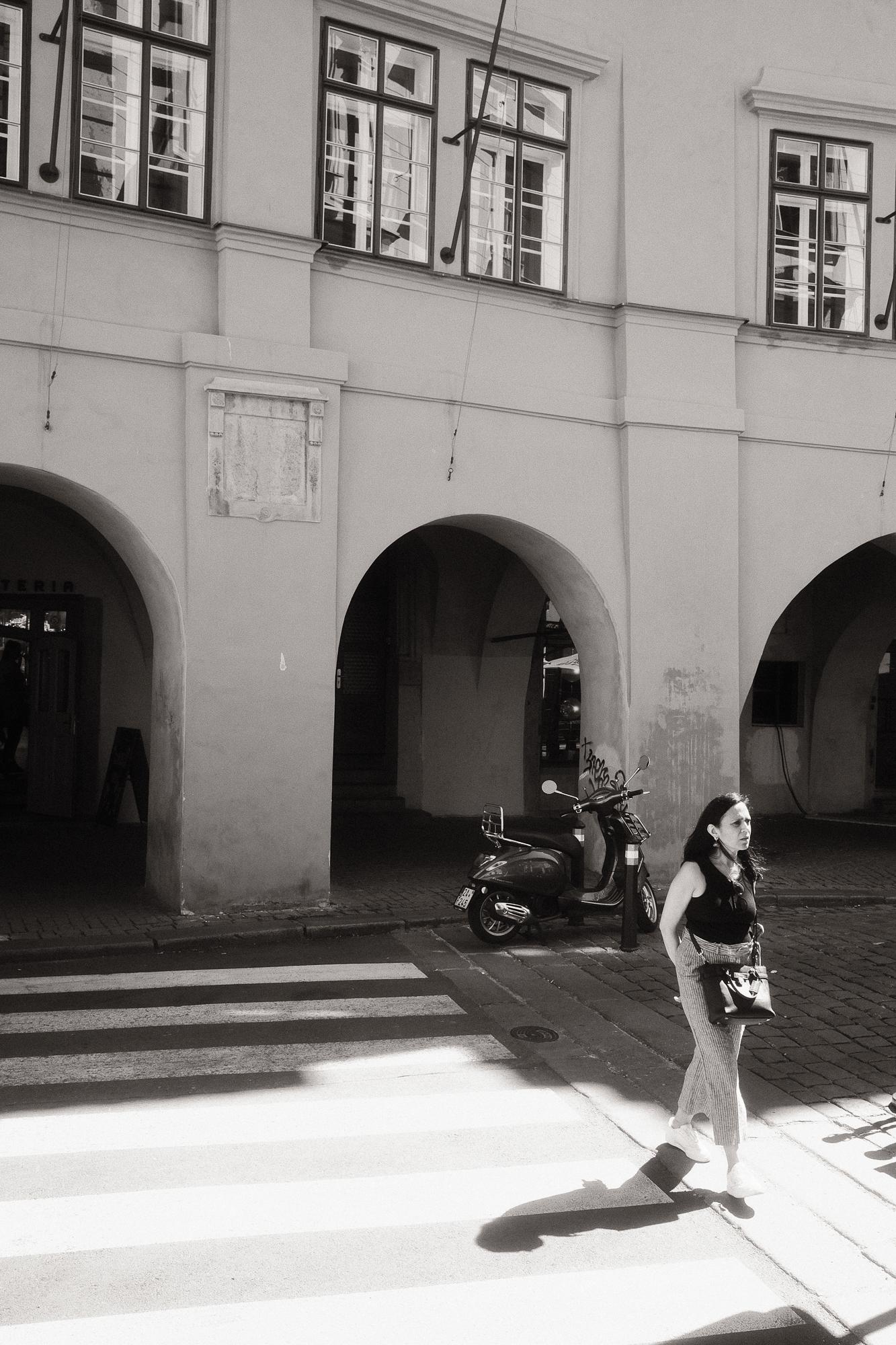 Čiernobiela fotografia čakajúcej pri zaparkovanej Vespe.