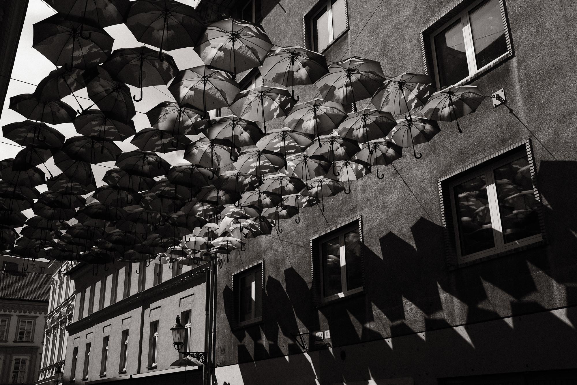 Ulice mesta s množstvom zavesených dáždnikov vytvárajúce geometrické vzory tieňov na stenách budov.