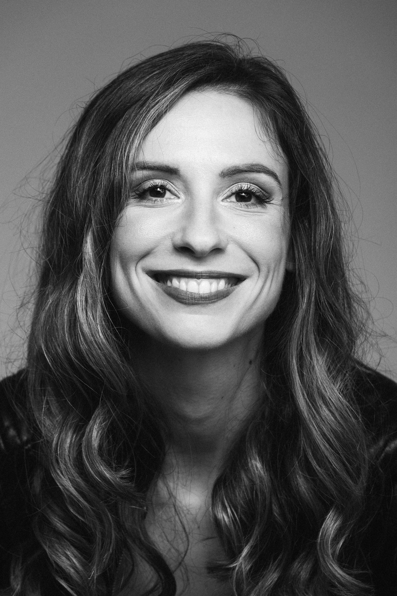 Čiernobiela fotografia mladej usmiatej ženy s dlhými vlnitými vlasmi pri jemnom osvetlení.