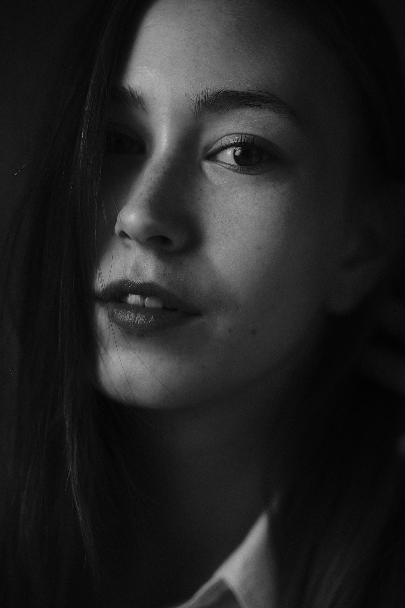 Čiernobiely detailný portét mladej ženy s emotívnym výrazom, jej jemne osvetlená tvár je čiastočne zakrytá prameňmi vlasov. Ateliér Pezinok