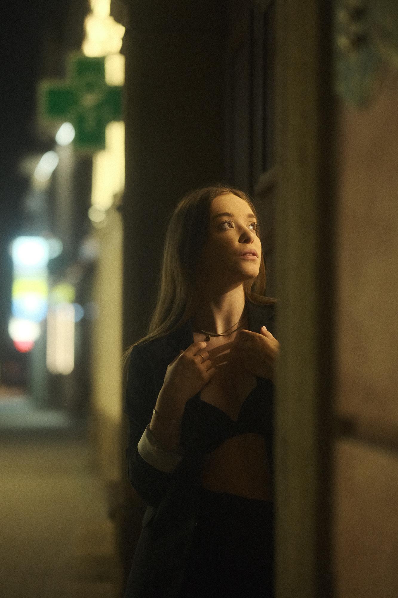 Portrét mladej ženy na nočnej ulici osvetlenej pásom svetla z brány do budovy. Pezinok.