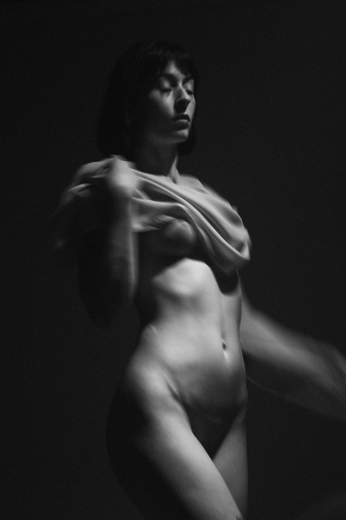 Čierno-biely umelecký akt zobrazujúci ženskú postavu, jemne osvetlenú, pri umeleckom pohybe s látkou. Ateliér Pezinok.