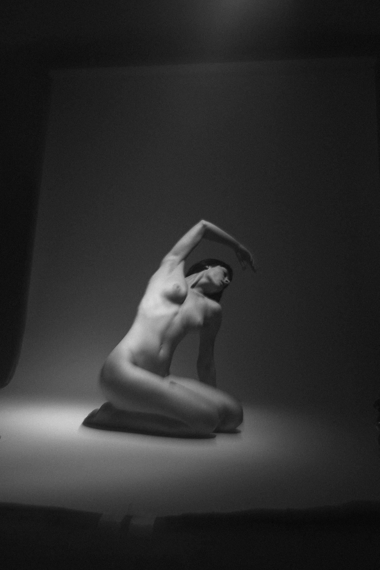 Čierno-biely umelecký akt zachytáva postavu sediacu na podlahe s hlavou dozadu a so zdvihnutou rukou. Fotografia vyžaruje eleganciu a jemnosť. Ateliér Pezinok.